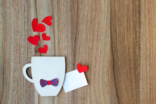 Decorative Cup with bow-tie and hearts on wooden background. Greeting card