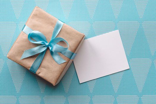 Gift box with blue ribbon on blue background wih greeting card.