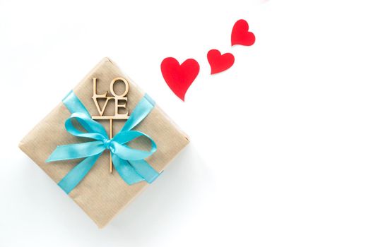 Gift box wrapped in brown paper with blue ribbon on white background. Top view. Flat lay