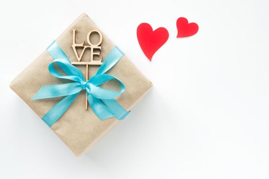Gift box wrapped in brown paper with blue ribbon on white background. Top view. Flat lay