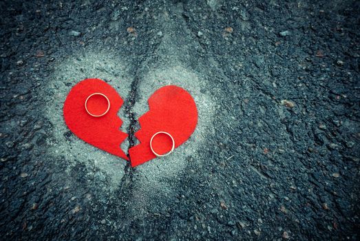 Divorce concept - broken red heart with wedding rings on cracked asphalt. Toned