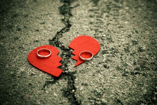 divorce concept - broken heart with wedding rings on cracked asphalt