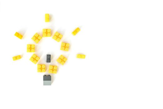 Idea concept. Lamp made of yellow plastic constructor bricks on white background. Popular toys.