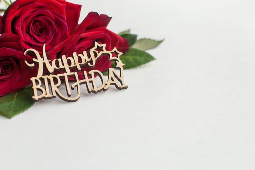 Composition of bouquet of red roses and decorative wooden greeting on white background. Happy Birthday. Space for text. Copyspace