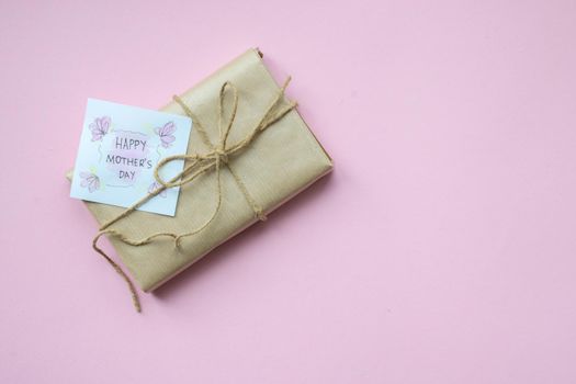 Presents wrapped in brown craft paper and tie hemp string on Light pink background. Gift box with greetings on Mothers Day. Top view. Copyspace
