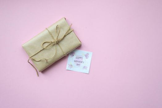 Presents wrapped in brown craft paper and tie hemp string on Light pink background. Gift box with greetings on Mothers Day. Top view. Copyspace