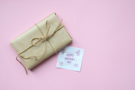 Presents wrapped in brown craft paper and tie hemp string on Light pink background. Gift box with greetings on Mothers Day. Top view. Copyspace