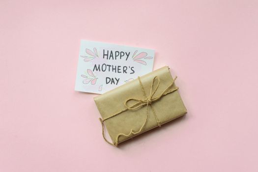 Presents wrapped in brown craft paper and tie hemp string on Light pink background. Gift box with greetings on Mothers Day. Top view. Copyspace