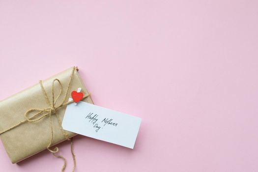 Presents wrapped in brown craft paper and tie hemp string on Light pink background. Gift box with greetings on Mothers Day. Top view. Copyspace