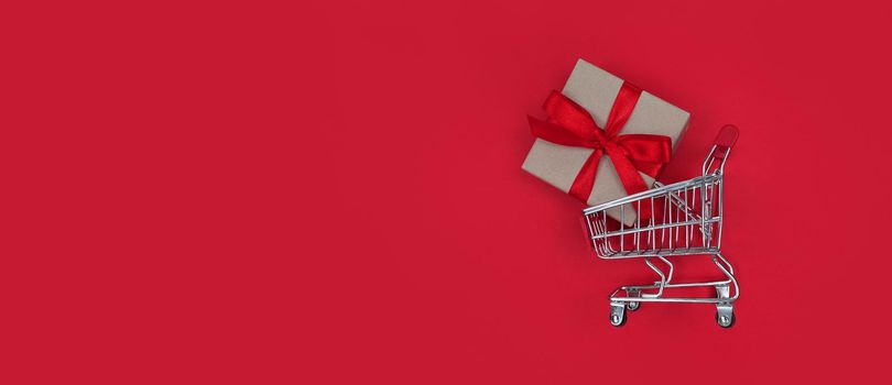 Supermarket trolley and gift box on a red background with copy space. Shopping concept.