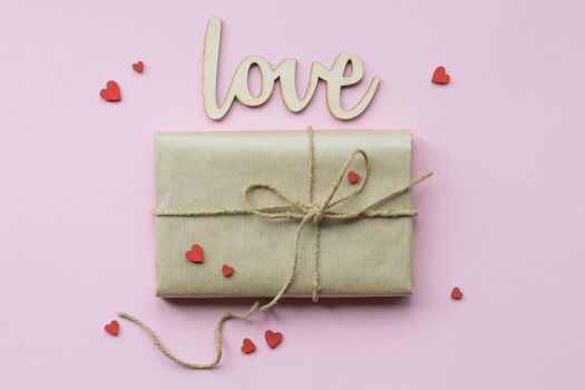 Present wrapped in brown craft paper and tie hemp string on Light pink background. Gift box with decorative red hearts for Mothers Day, Wedding, Birthday and Valentines Day. Top view. Copyspace