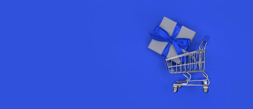 Supermarket trolley and gift box on a blue background with copy space. Shopping concept.