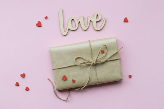 Present wrapped in brown craft paper and tie hemp string on Light pink background. Gift box with decorative red hearts for Mothers Day, Wedding, Birthday and Valentines Day. Top view. Copyspace