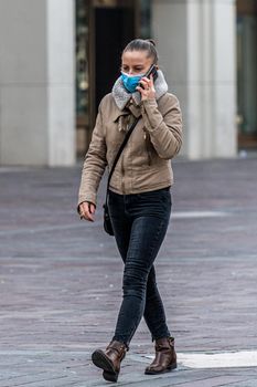 terni,italy february 05 2021:woman walking in the city with medical mask and using smartphone