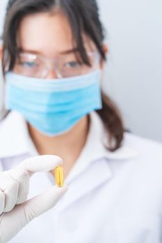 Close up Scientist hands putting in nitrile latex gloves holding Omega 3 capsule in labcoat wearing nitrile gloves, doing experiments in lab