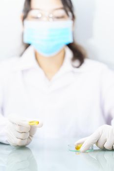 Close up Scientist hands putting in nitrile latex gloves holding Omega 3 capsule in labcoat doing experiments in lab