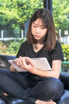 Young girl studying online from digital tablet on the sofa in parlor at home