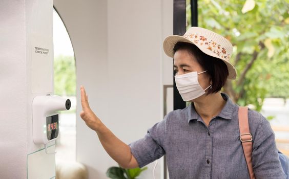 Female tourist use wall infrared thermometer before enter restaurant