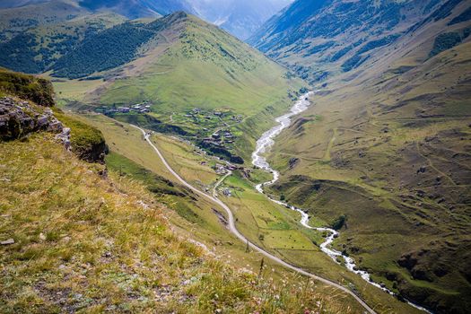 Majestic mountains of the Caucasus with a beautiful view. Green vegetation and shrubs on smooth plains. The river flows along the road. Magnificent mesmerizing landscape.