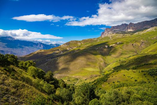 High mountains of the Caucasus with beautiful views. Green vegetation and dense forest above a blue sky. A great fascinating landscape.