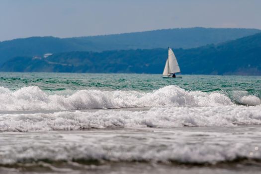 Seascape, small waves with white foam at the top against the background of blue water. A lone sailboat can be seen in the distance. A great place to relax and reflect