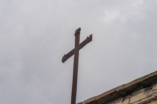 cross placed on the tip of a church roof with gray sky background