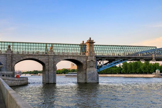 A large powerful bridge over the river, the top of the space is covered with glass. Big concrete columns, a ship floating under the bridge.