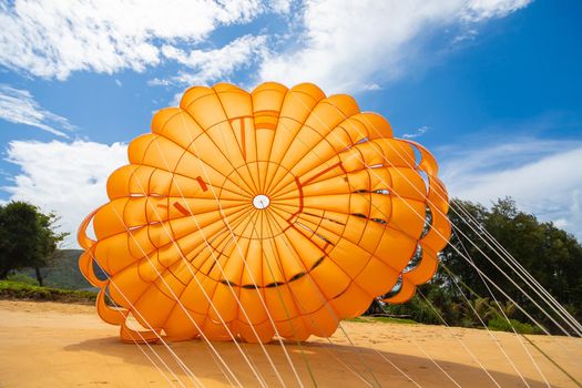 A bright orange parachute lies on the sand near the water to attract people to fly and look at the sea from a height.