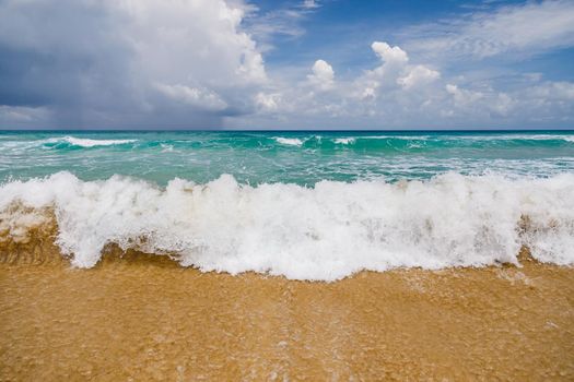 Powerful, stormy, foamy waves are picked up by the wind. White foam from bubbles of different sizes is scattered to the sides and spreads all over the beach. Close-up.
