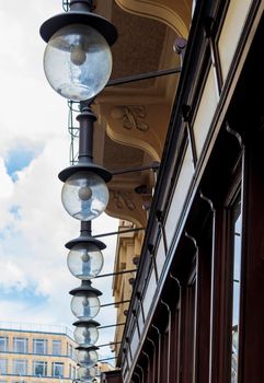 Round lanterns, inside an electric lamp, on metal mounts hang on the facade of the building, under the roof canopy.