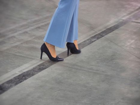 Woman step legs wearing black high heels shoes on concrete floor close up view