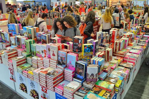 Couple of female teen friends surrounded by books at publishing house booth in international book fair