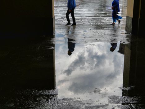 People silhouettes reflected in puddle of water after the storm