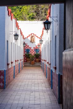 Hall in Mexico City with white walls, classic hanging lamps, and plants at the end. Long corridor with brown tiled floor and classic Hispanic architecture. Colorful Mexican neighborhood