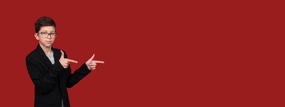 cute boy with glasses, pointing his hands to empty place isolated on red, burgundy background. copy space. . High quality photo