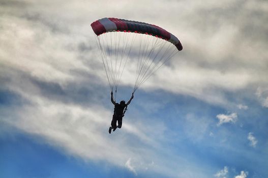 Parachutist silhouette on blue cloudy sky