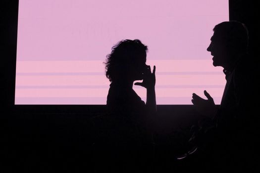 Silhouette of a couple talking and gesturing on a pink background