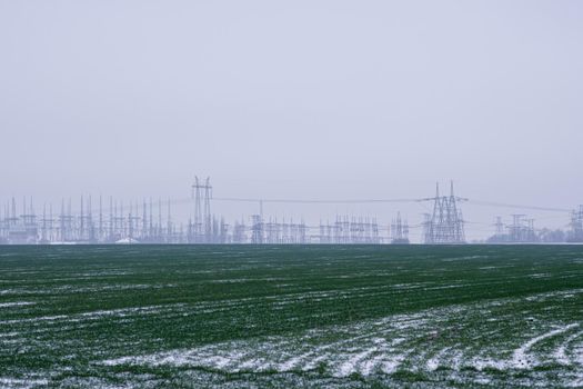 agricultural landscape in the Ukraine with high voltage power lines and a with cloudy skies. Winter wheat field with snow in winter in Europe. High quality photo