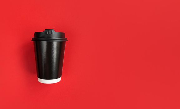 Black paper coffee cup to go on a red background with copy space.