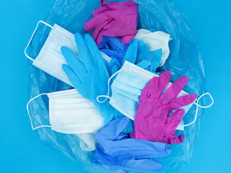 Medical pandemic coronavirus waste, face masks and latex gloves in garbage bag on a blue background.