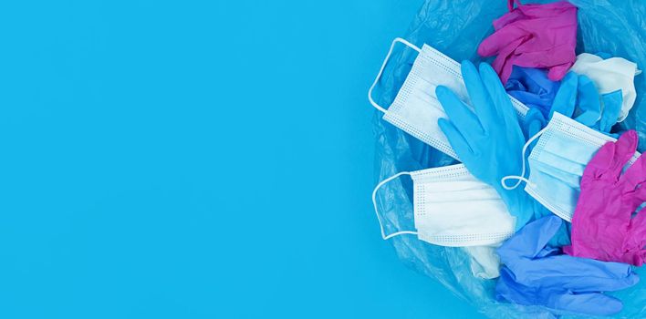 Medical pandemic coronavirus waste, face masks and latex gloves in garbage bag on a blue background with copy space.