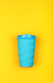 Close up one crimped disposable pastel blue paper takeaway coffee cup over vivid yellow background, flat lay, elevated top view, directly above