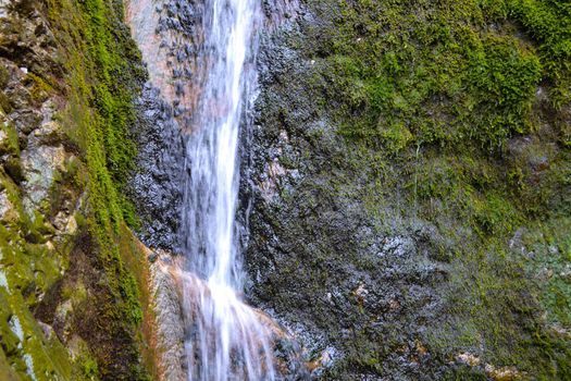 Small waterfall on a rocky stream stone background. Mountain covered with green moss.