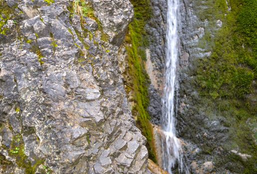 Small waterfall on a rocky stream stone background. Mountain covered with green moss.