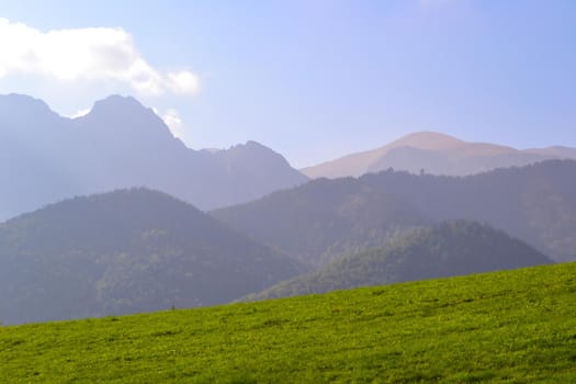 Green meadow in front of mountains in a slight haze. Spring nature and freshness. Beautiful background for advertising natural products