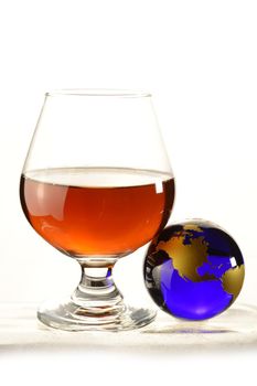 A globe and glass of Cognac over a white background.