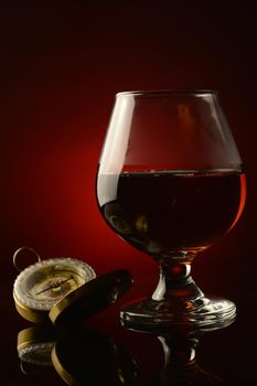 A vertical composition of a glass of Cognac and an old style compass over a dark atmospheric background.