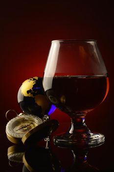A glass of Cognac with a compass and globe over a dark red and black background.