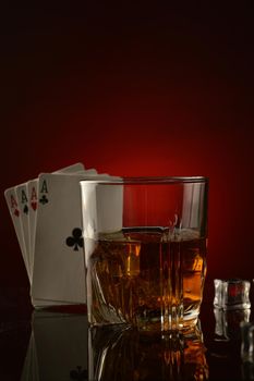 A shallow depth of field on the whiskey glass with four aces to represent a gambling mans drink.