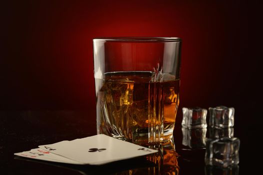A glass of whiskey and a made poker hand over a dark reflective red and black background.